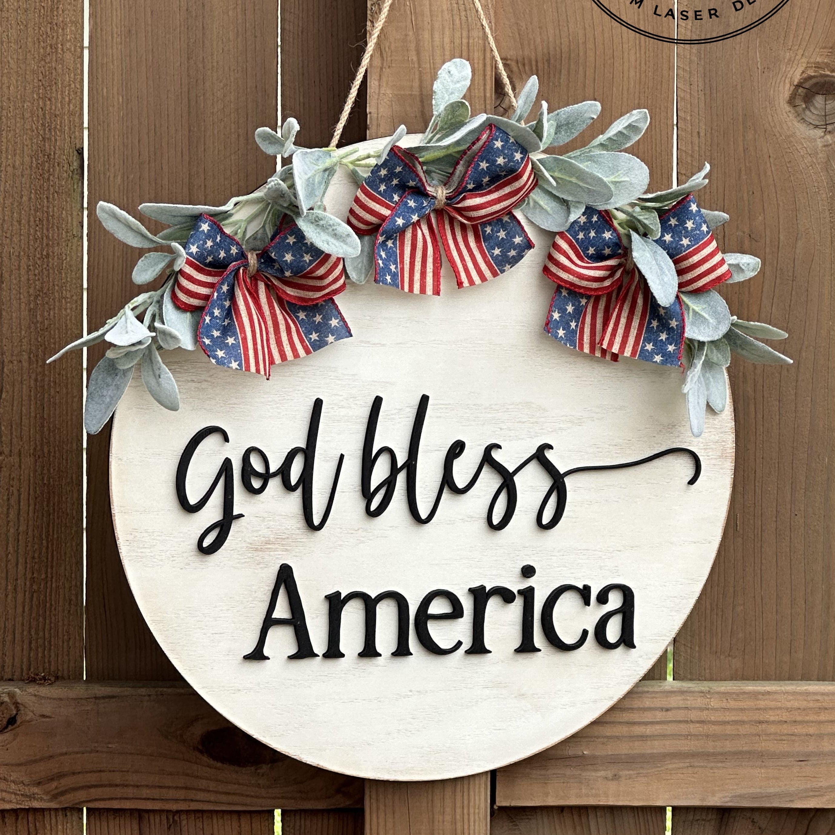 Decorative sign with 'God bless America' text and American flag ribbons on a wooden background.
